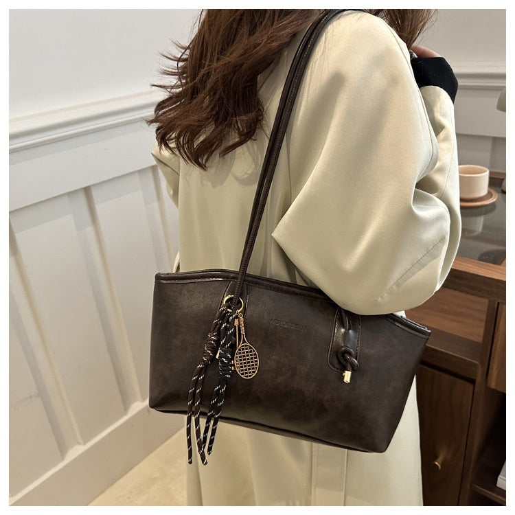 Person wearing a beige coat with a brown handbag featuring decorative elements.