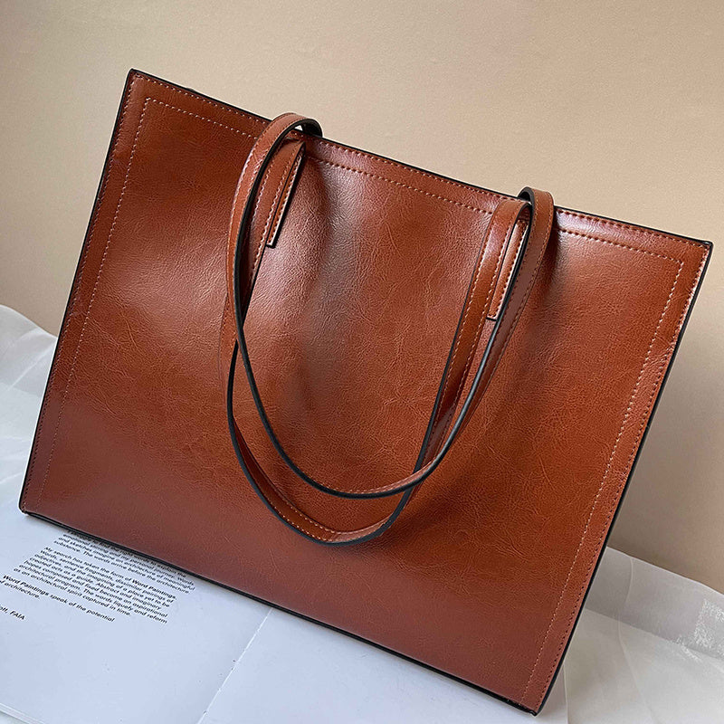 Brown leather tote bag on a light surface with a beige background