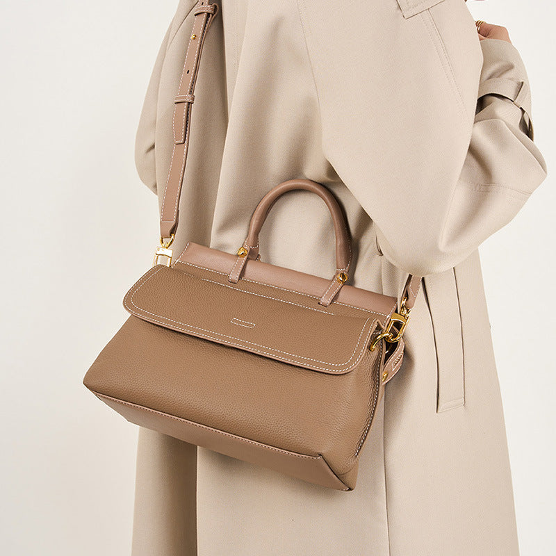 Beige handbag held by a person wearing a beige coat on a light background