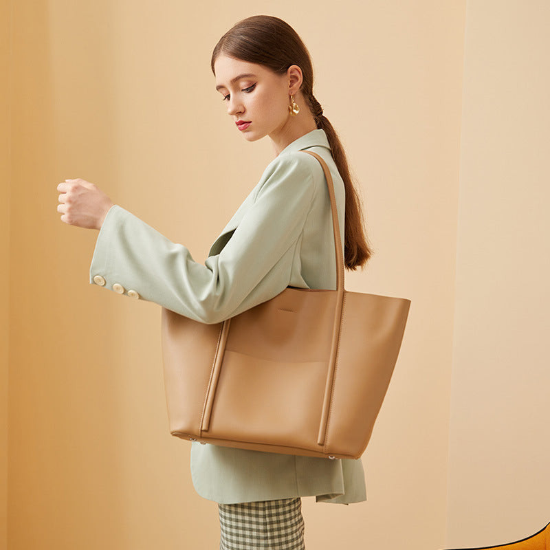 Woman holding a brown leather tote bag against a beige background